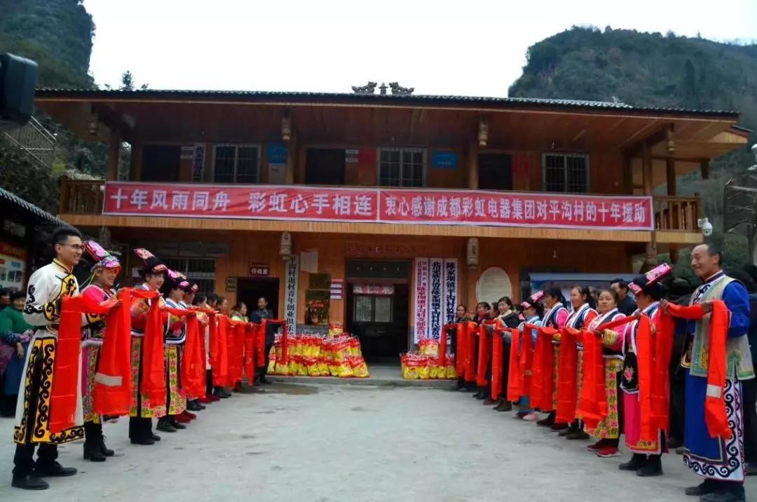 怀感恩之心，平沟村村民手持羌红在乐竞平台_乐竞（中国）公司援建的平沟村便民服务楼前热情等待乐竞平台_乐竞（中国）亲人们的到来